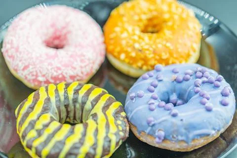 Four different doughnuts arranged on a black tray, each with unique glazes .. Stock Photos