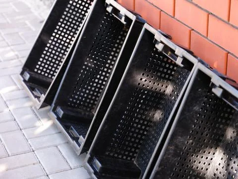 Four empty black plastic crates for fruits and vegetables standing leaning ag Fotos Stock