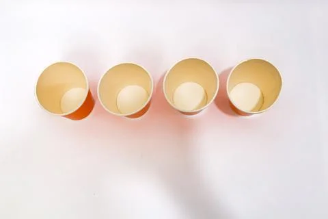 Four empty paper cups arranged in a row on a white surface, casting soft sh.. Stock Photos