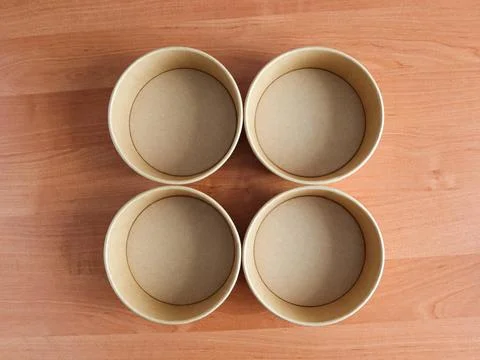 Four empty round paper containers on a wooden table Stock Photos