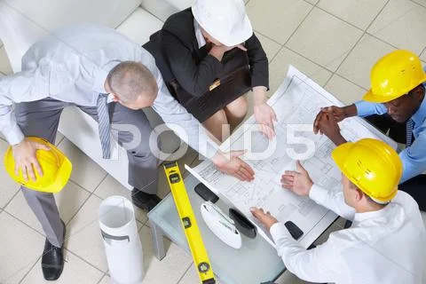 Four engineers sitting at table and discussing a blueprint Stock Photos
