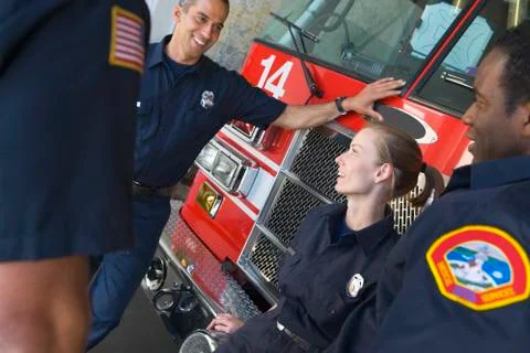 Four firefighters talking by fire engine Stock Photos