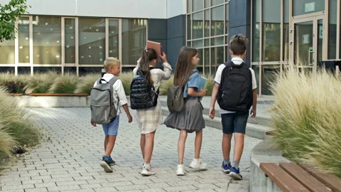 Four first graders, two boys and two girls, approach the school building Stock Footage 229254479