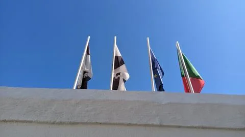 Four flags on top of four pillars of their metal against a blue sky Portugal Stock Photos