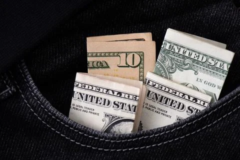 Four folded US dollar banknotes stick out in the pocket of black jeans. 스톡 사진