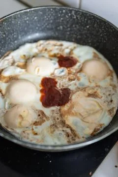 Four fried eggs are being cooked in a black speckled frying pan Stock Photos