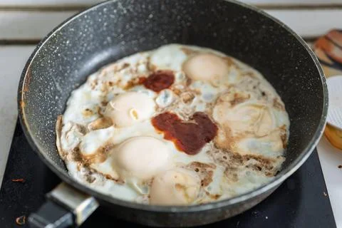 Four fried eggs are being cooked in a black speckled frying pan Stock Photos