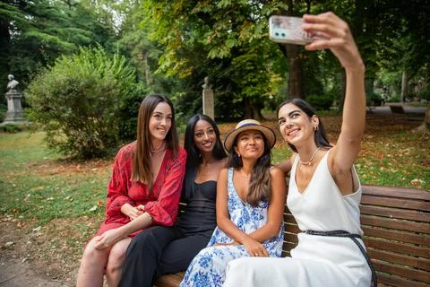 Four friends are sitting on a patch in a public park and taking a selfie to.. Stock Photos