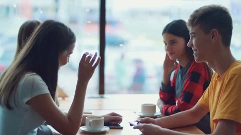 Four friends are sitting at a table in a cafe and chatting Stock Footage 143964291