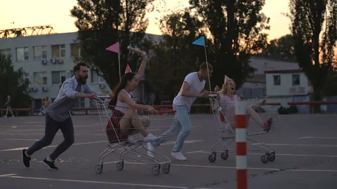 Four friends having fun together. Running at the car parking with trolleys. Stock Footage 110301526