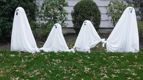 Four ghosts standing in a row on a lawn outside for Halloween Stock Photos