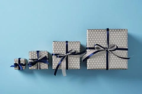 Four gift boxes of different sizes are lined up on a pastel blue background.. Stock Photos