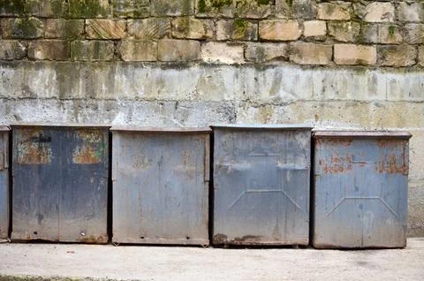 Four gray rusty trash bins with a background of an old brick wall. Stock Photos