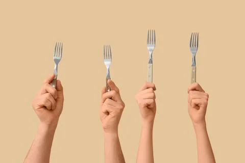 Four hands holding up silver forks with wooden handles against a solid beige  Stock Photos