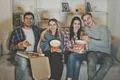 The four happy friends with a popcorn and a pizza watch a film on the sofa Photo