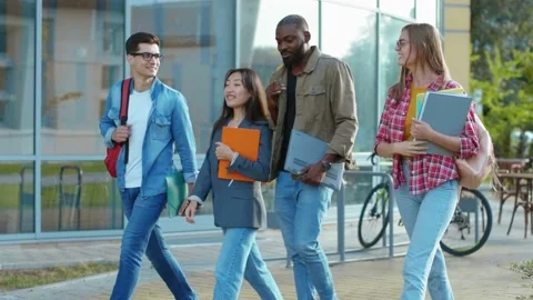 Four happy multi-ethnic friends walking out of campus university talk loudly Stock Footage 140781006