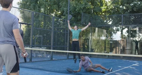 Four men, purple-shirted man lunging, returning low ball with paddle on blue Stock Footage 342067040