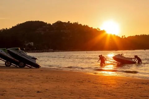 Four mens at sunset pull hydrocycle out of the water. Workers of the beach. W Stock Photos