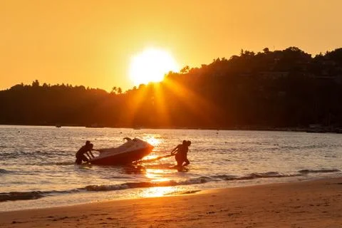 Four mens at sunset pull hydrocycle out of the water. Workers of the beach. W Stock Photos