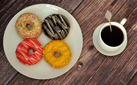 Four multi-colored glazed doughnuts with toppings on a round plate and a cu.. Stock Photos