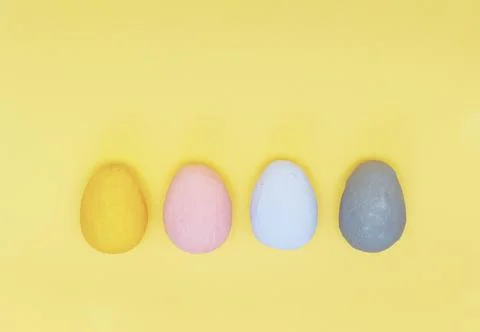 Four multi-colored handmade eggs on a light-yellow background. Stock Photos