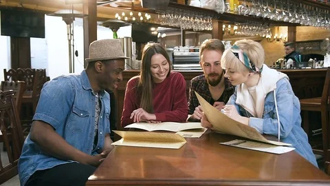 Four multi ethnic friends choosing dishes from menu in the bar, pub. Stock Footage 109157484