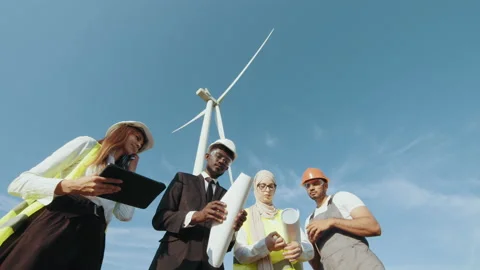 Four multi ethnic partners in safety helmets studying wind turbine blueprints Stock Footage 170581146