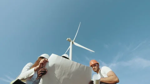 Four multi ethnic partners in safety helmets studying wind turbine blueprints Stock Footage 170581597