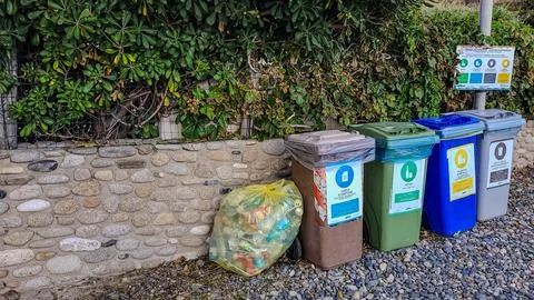 Four multicolored garbage sorting containers and one yellow bag in the beach Stock Photos