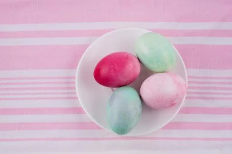 Four multicolored painted Easter eggs on a white plate and  striped pink-whit Stock Photos