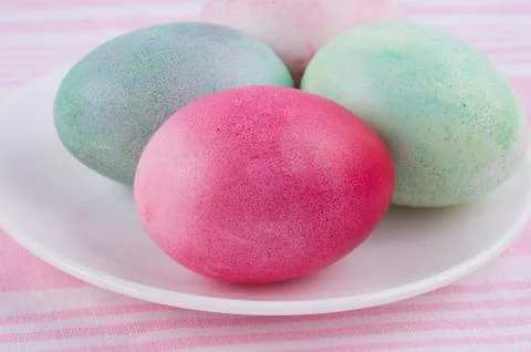 Four multicolored painted Easter eggs on a white plate and  striped pink-whit Stock Photos