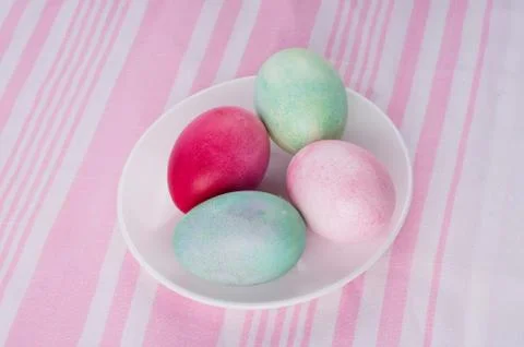 Four multicolored painted Easter eggs on a white plate and  striped pink-whit Stock Photos