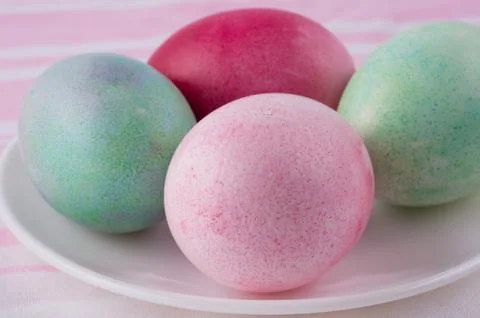 Four multicolored painted Easter eggs on a white plate and  striped pink-whit Stock Photos