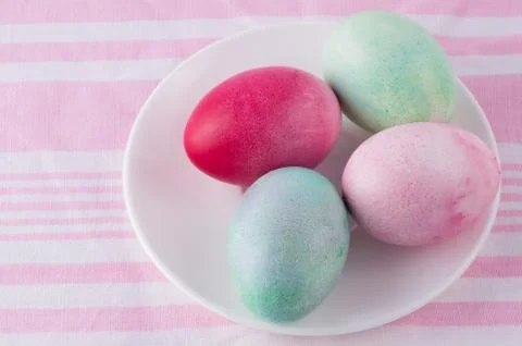 Four multicolored painted Easter eggs on a white plate and  striped pink-whit Stock Photos