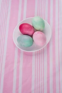 Four multicolored painted Easter eggs on a white plate and  striped pink-whit Stock Photos