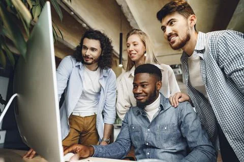 Four multiethnic colleagues looking at computer screen in office Stock Photos