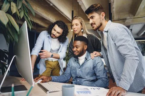 Four multiethnic colleagues looking at computer screen in office Stock Photos