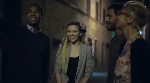 Four multiethnic friends are chattering at night in old town centre alley Stockbeeldmateriaal 64518728