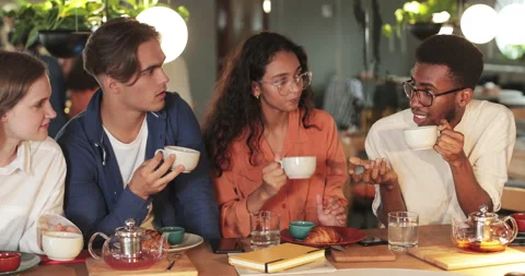 Four multiethnic friends drinking tea and talking while having lunch. Cheerful Stock Footage 137494524