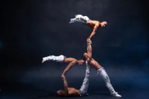 Four muscular man perform difficult acrobatic tricks on black studio Stock Photos