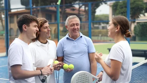 Four paddle tennis players of different ages friendly talking on outdoor court Stock Footage 323068366