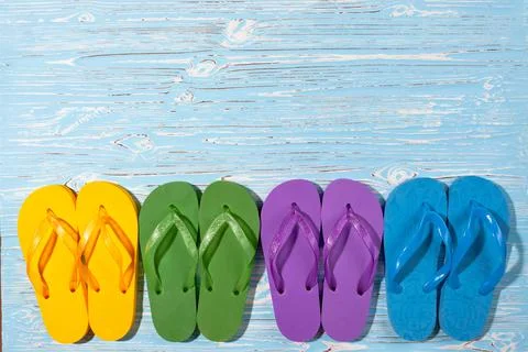 Four pairs of multi-colored rubber beach flip flops on a blue wooden background Stock Photos