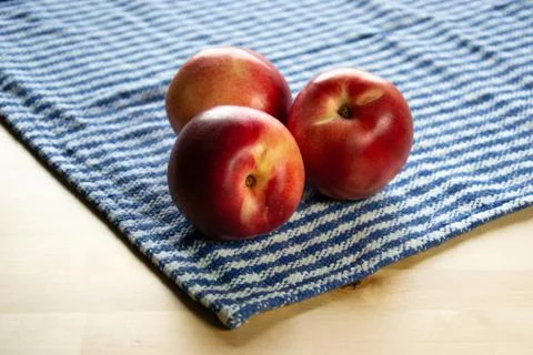 Four peaches on the table with tablecloth. Stock Photos