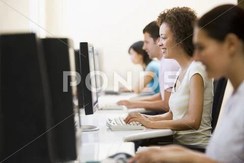 Four people in computer room typing and smiling Stock Photos