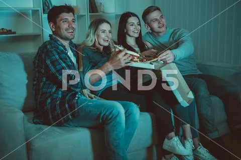 The four people eat a pizza and watch a movie on the sofa Stock Photos