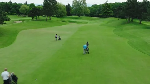 Four people Playing Golf walking with their chariots of golf clubs towards green Video stock 243525754