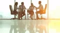 The four people sit at the table and talk on the background of the bright sun 4k or 4k+ Resolution