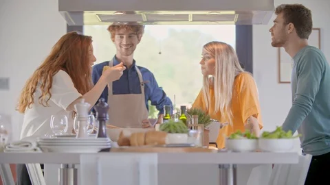 Four people talking while cooking together at home in modern kitchen.Young 스톡 동영상 129033343