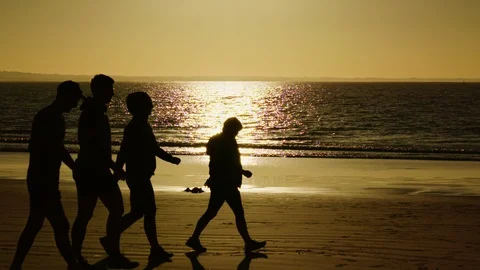 Four people walking on a beautiful beach at sunrise in slow motion. Stock Footage 86881590