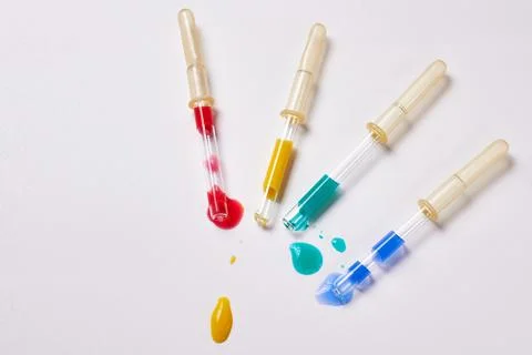 Four pipettes with a multi-colored liquid on a white background. Stock Photos
